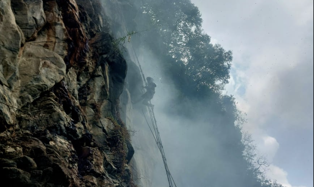 Buddhi dai hanging from rope on cliff with smoke rising